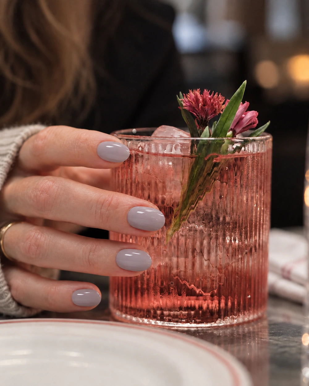 Hånd med taupefargede, ovale negler holder et cocktailglass